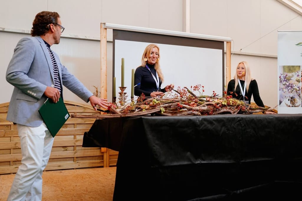 Pokaz florystyczny na scenie Baltic Flora: prowadzący i dwie florystki przy długiej kompozycji z gałęzi i świec